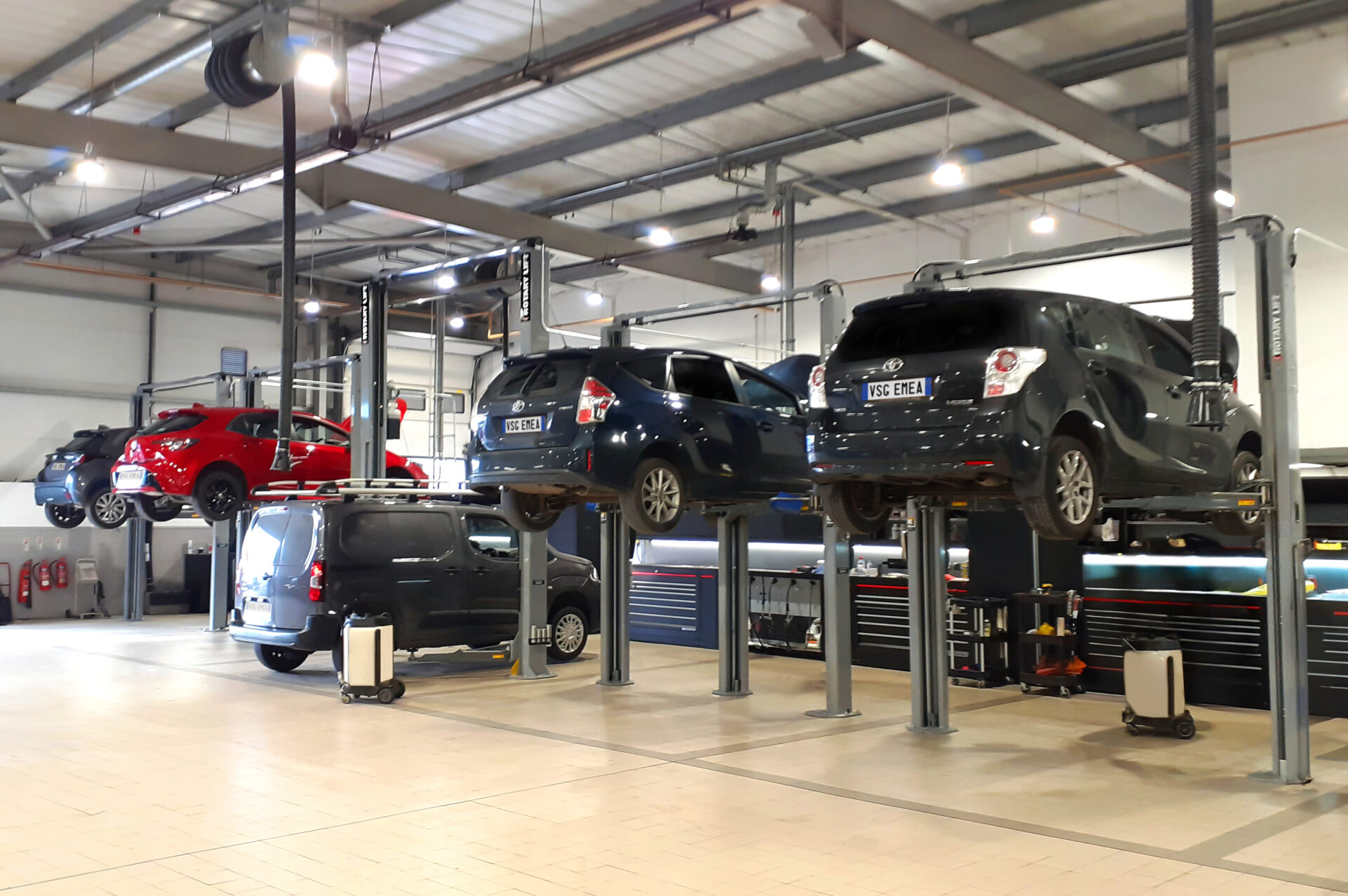 Five cars are serviced and lifted by two-column lifts in a workshop