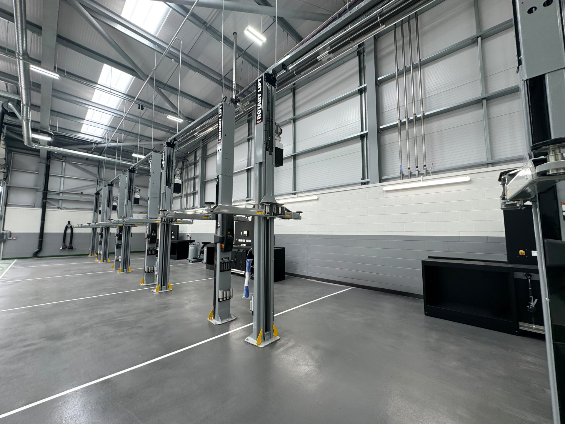 A range of Rotary two-post lifts are positioned in a gray dealership workshop