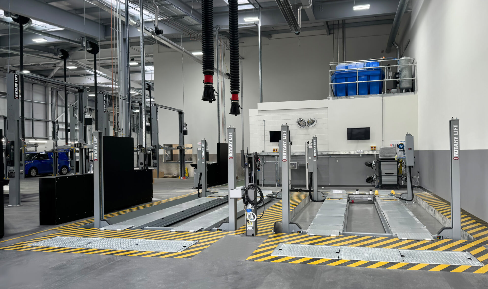 Two gray Rotary four-post lifts are positioned inside a dealership's repair shop