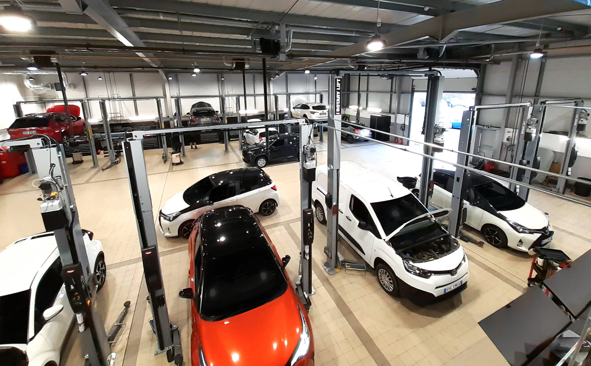 Wide-angle overview of a repair shop where several cars and a series of car lifts are parked