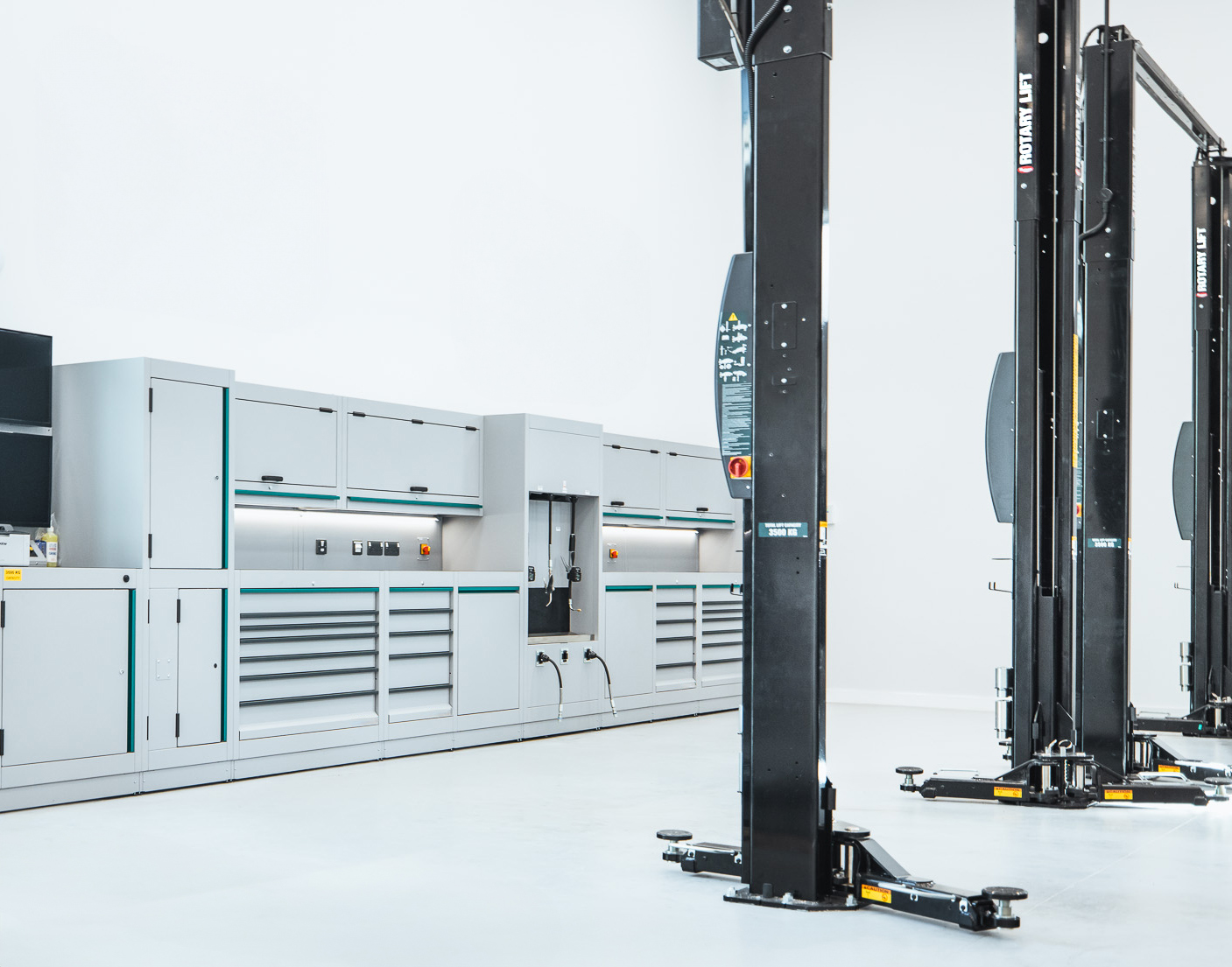 A pair of black Rotary 2-post lifts positioned in front of garage work shelves in a workshop