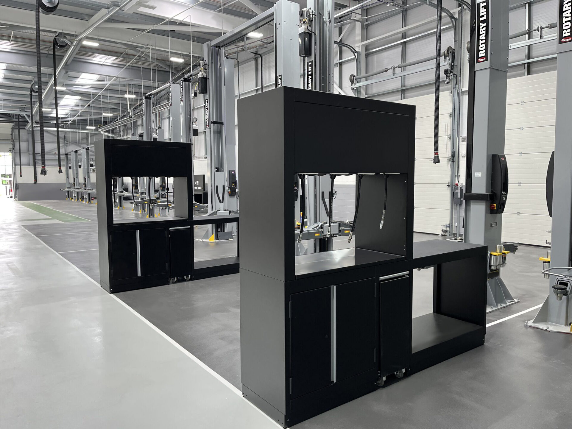 Two black workshop work benches are positioned in front of their respective gray Rotary car lifts