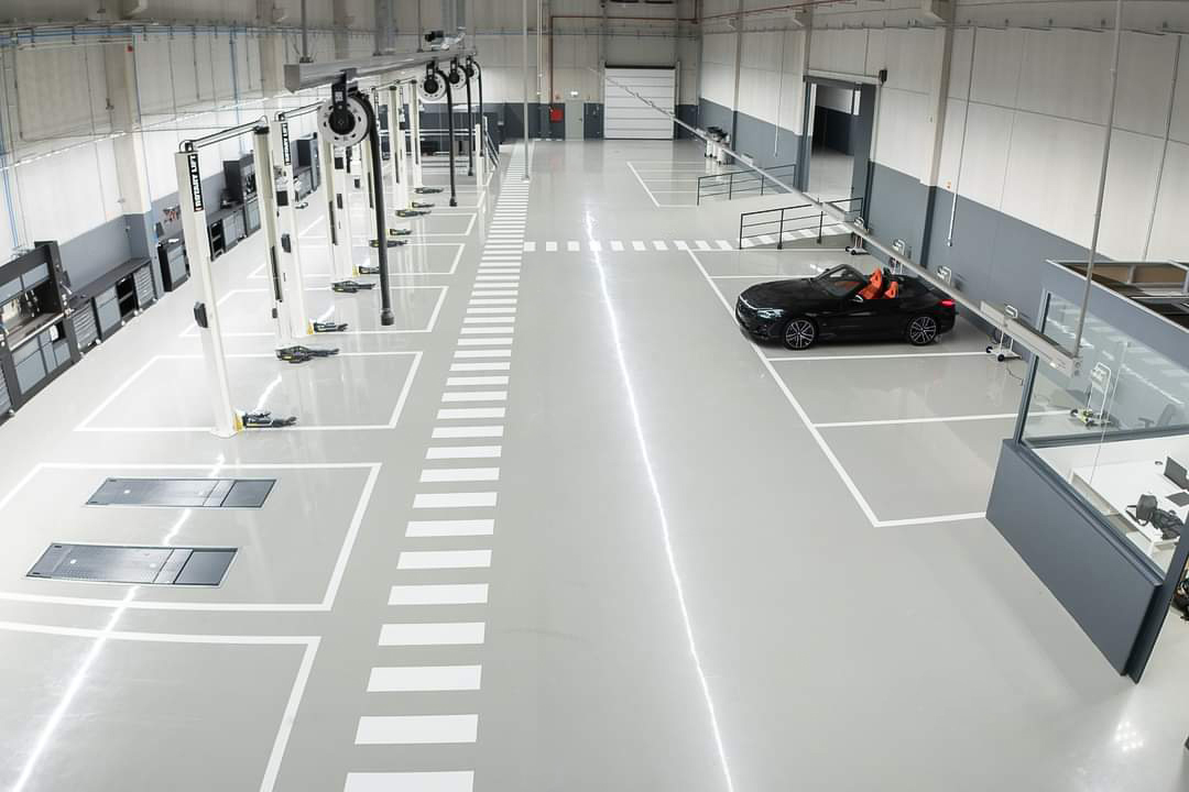 Top view of a car dealership garage that on the left is equipped with car lifts and on the right is parked a black car and an access ramp.