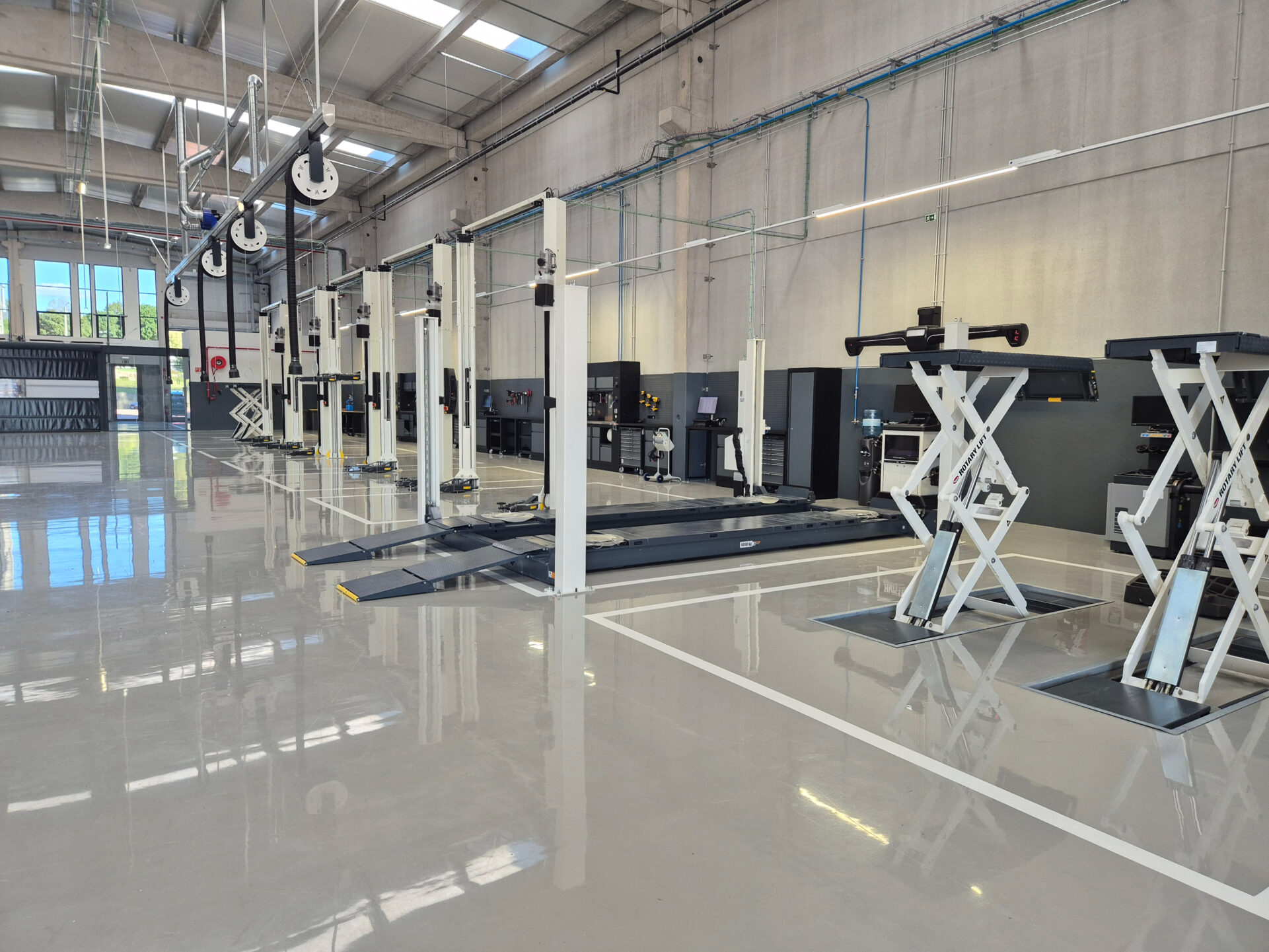 Two white double scissor lifts, one 4-post lift, and four white two-post lifts are placed in the workshop of a dealership