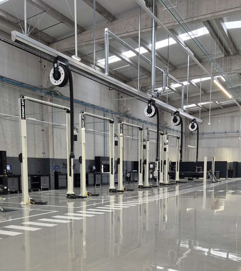Four white two-post lifts Rotary Lift branded are positioned in a garage with polished floors and workshop equipment